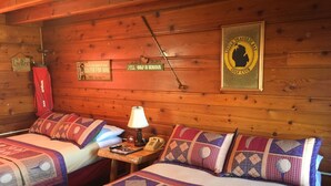 A cabin-style room with two beds, a lamp, a telephone, and a framed sign on the wall.