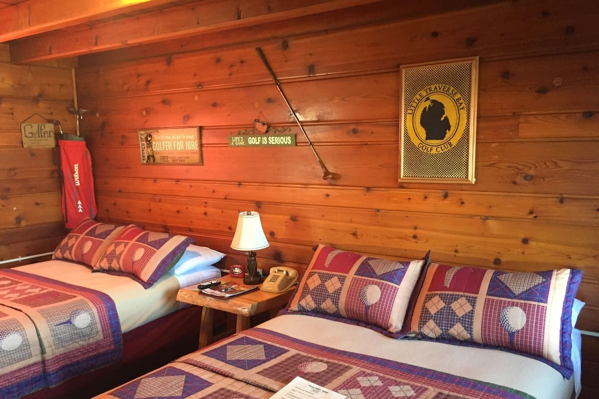 A cabin-style room with two beds, a lamp, a telephone, and a framed sign on the wall.
