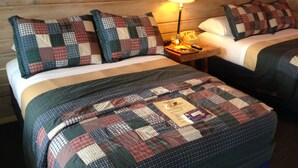 A room with two beds, each with a checkered bedspread and pillows, a nightstand with a lamp, and a wooden headboard. - The Waters Inn (Gaylord)