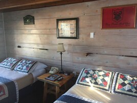 Quarto de hotel com duas camas, uma mesinha com abajur, quadro decorativo com tema de golfe e uma placa na parede.
