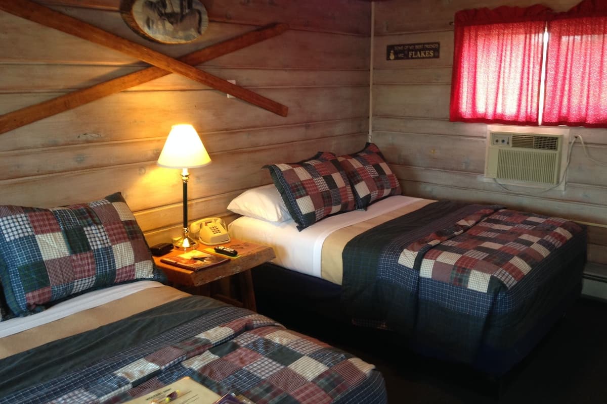 A cozy cabin room with two beds, a lamp, a telephone, and a sign on the wall.