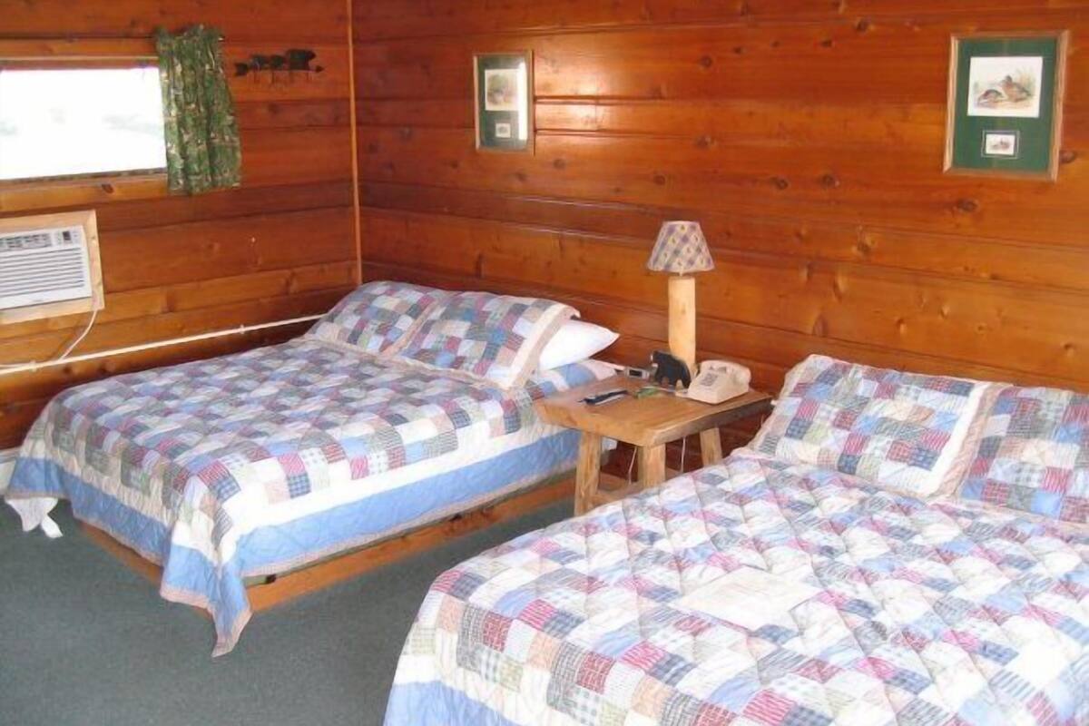 A cabin room with two beds, a small table, a lamp, and a window with curtains.