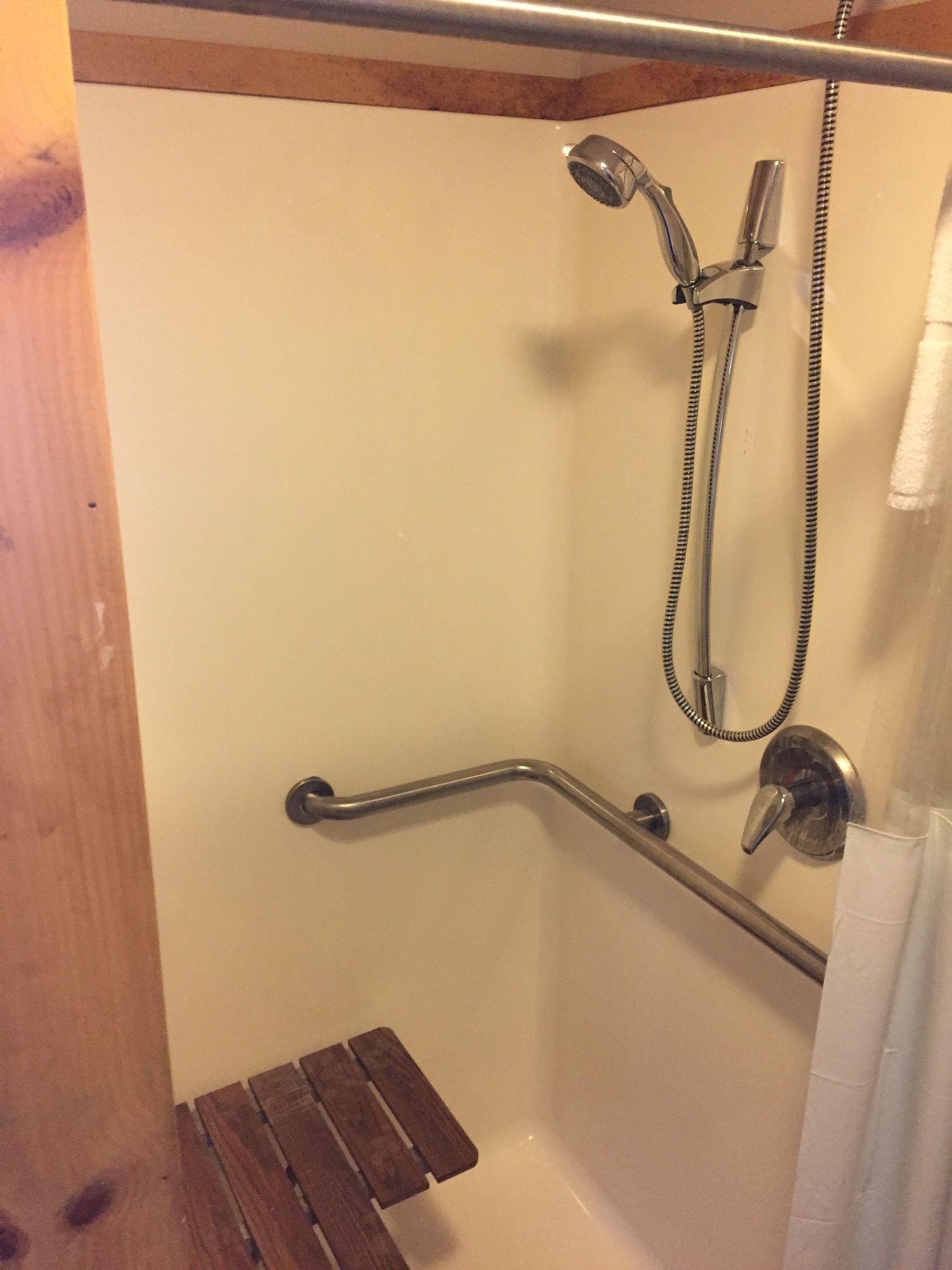 A shower area with a grab bar, a handheld showerhead, and a towel rack.