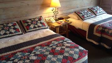 Una habitación acogedora con dos camas, cada una con una colcha acolchada y almohadas a juego. Un mesita de noche de madera con una lámpara y un teléfono está entre las camas.