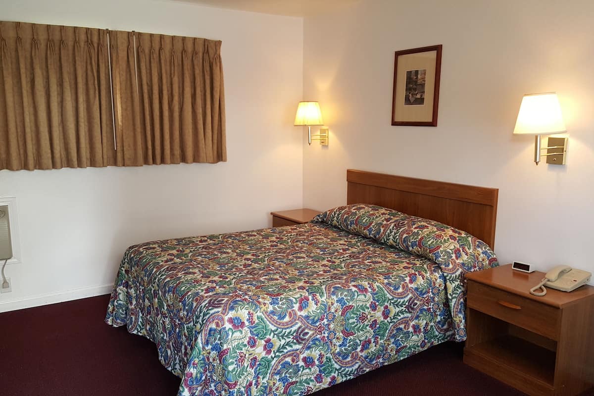 A hotel room with a bed, a bedside table with a lamp, a phone, and an air conditioning unit.