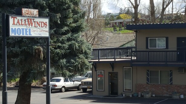 Un motel appelé Tall Winds, avec un panneau indicateur, un bâtiment doté d’un balcon et des voitures garées.