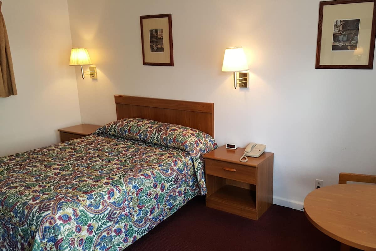 A hotel room with a bed, bedside table with a lamp, a small table, and two framed pictures on the wall.