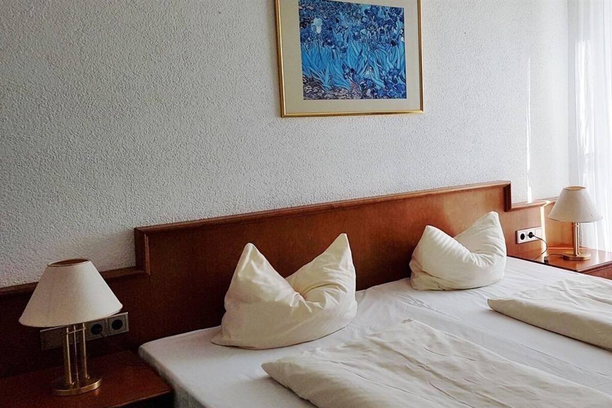 A hotel room with a wooden headboard, white bedding, and a framed artwork above the bed.