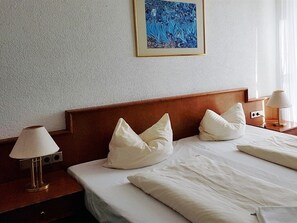 A hotel room with a wooden headboard, white bedding, and a framed artwork above the bed.