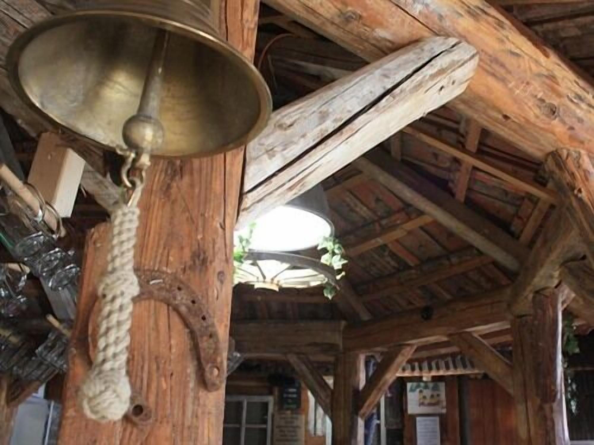 A rustic wooden structure with a metal bell hanging from a post.