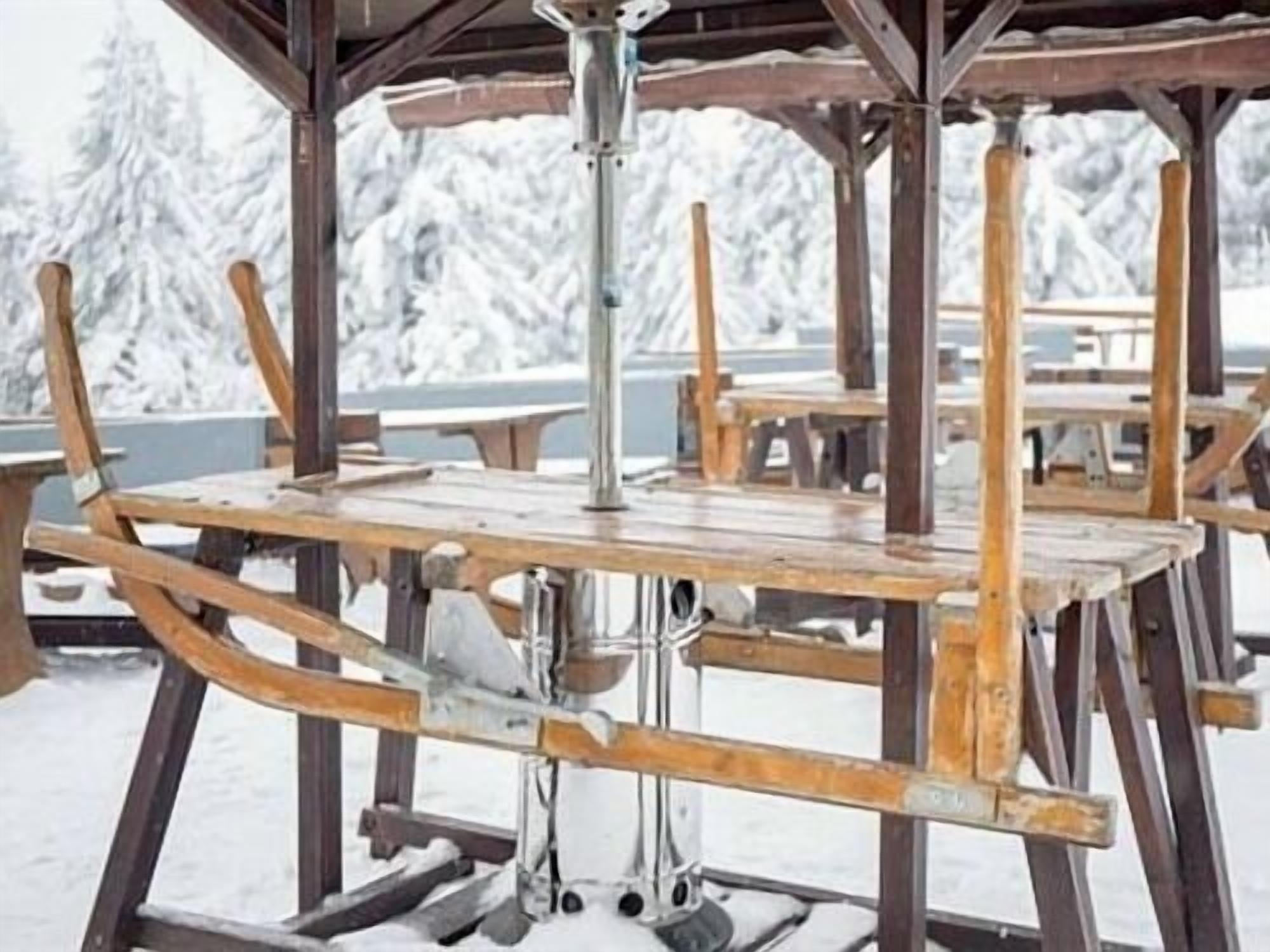 A wooden gazebo with metal supports, surrounded by snow-covered trees.