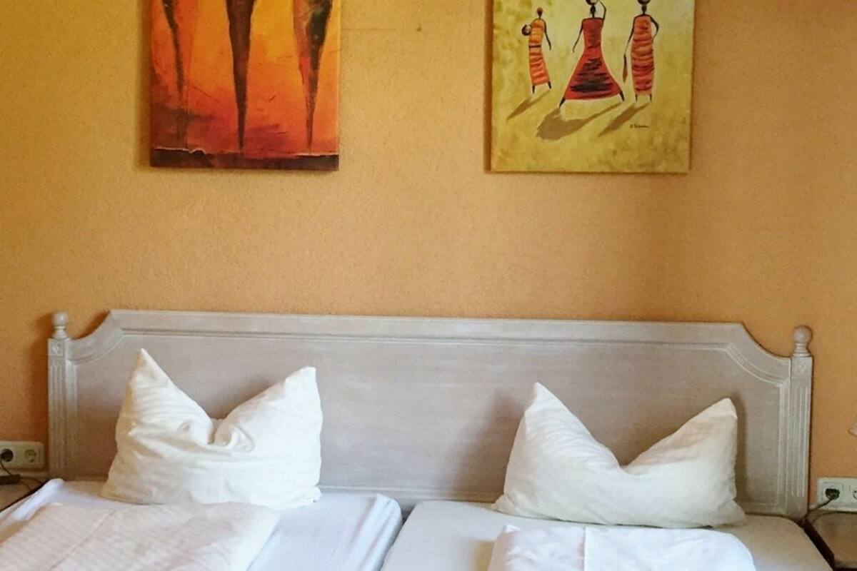 A hotel room with a double bed, white bedding, and two pillows. There are two paintings on the wall above the bed.