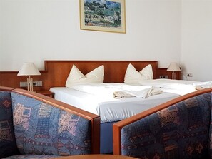 A hotel room with a large bed, two bedside tables with lamps, patterned armchairs, and a framed painting on the wall.