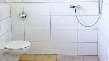 A small, tiled bathroom with a toilet, a shower, and a floor drain.