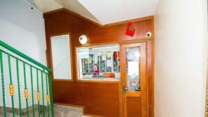 Un espace d’accueil avec une porte en bois, un comptoir de réception et une rambarde verte.