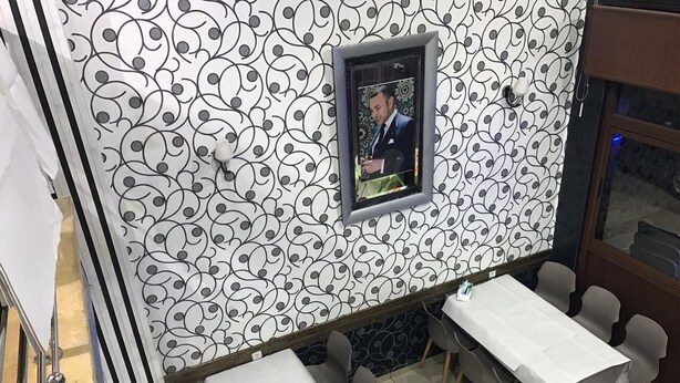 L’intérieur d’un restaurant, avec un mur orné de motifs, une photo encadrée et une table entourée de chaises.