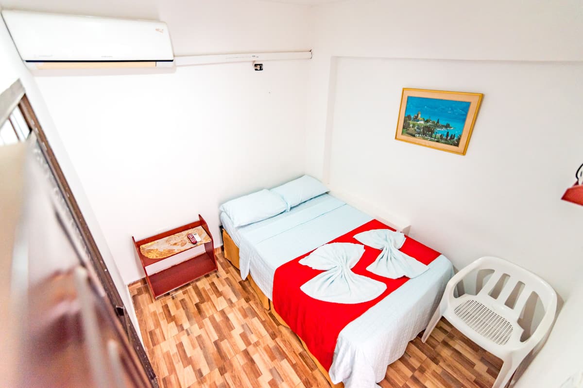 A small, clean room with a bed, a chair, a nightstand, and a picture on the wall.