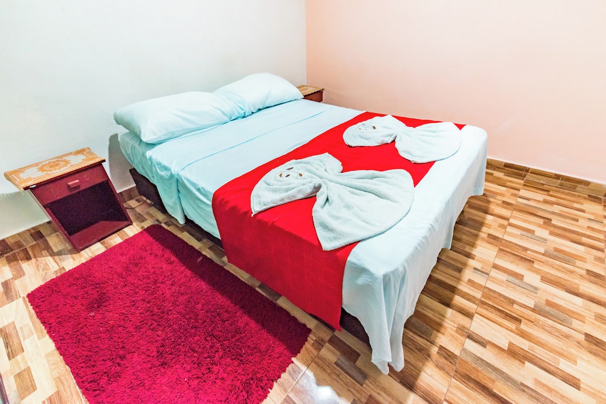 A neatly made bed with a red and white bedspread, two pillows, and two white bathrobes on the bed.