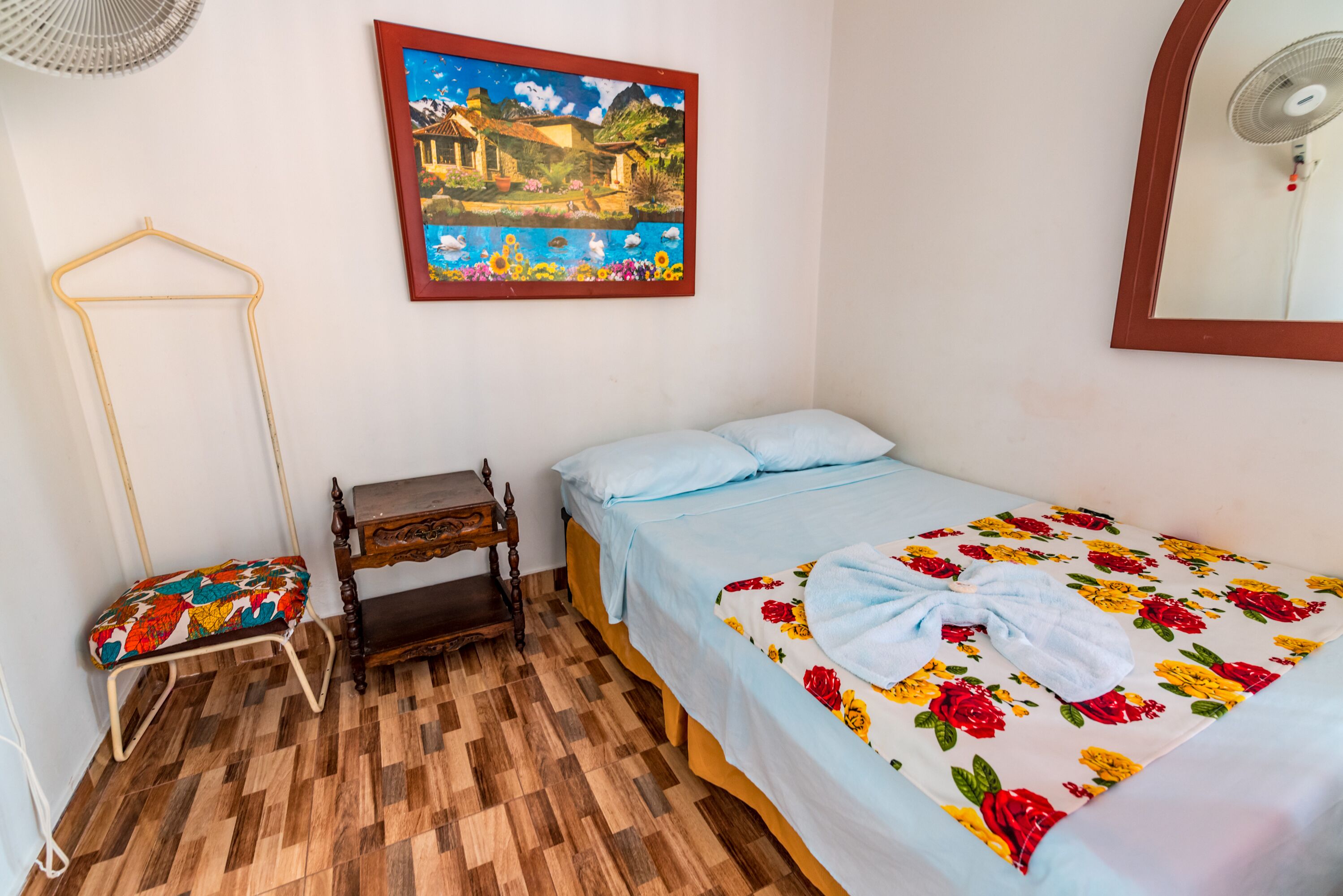 A bedroom with a bed, a wooden bench, a hanging chair, a painting, and a mirror.