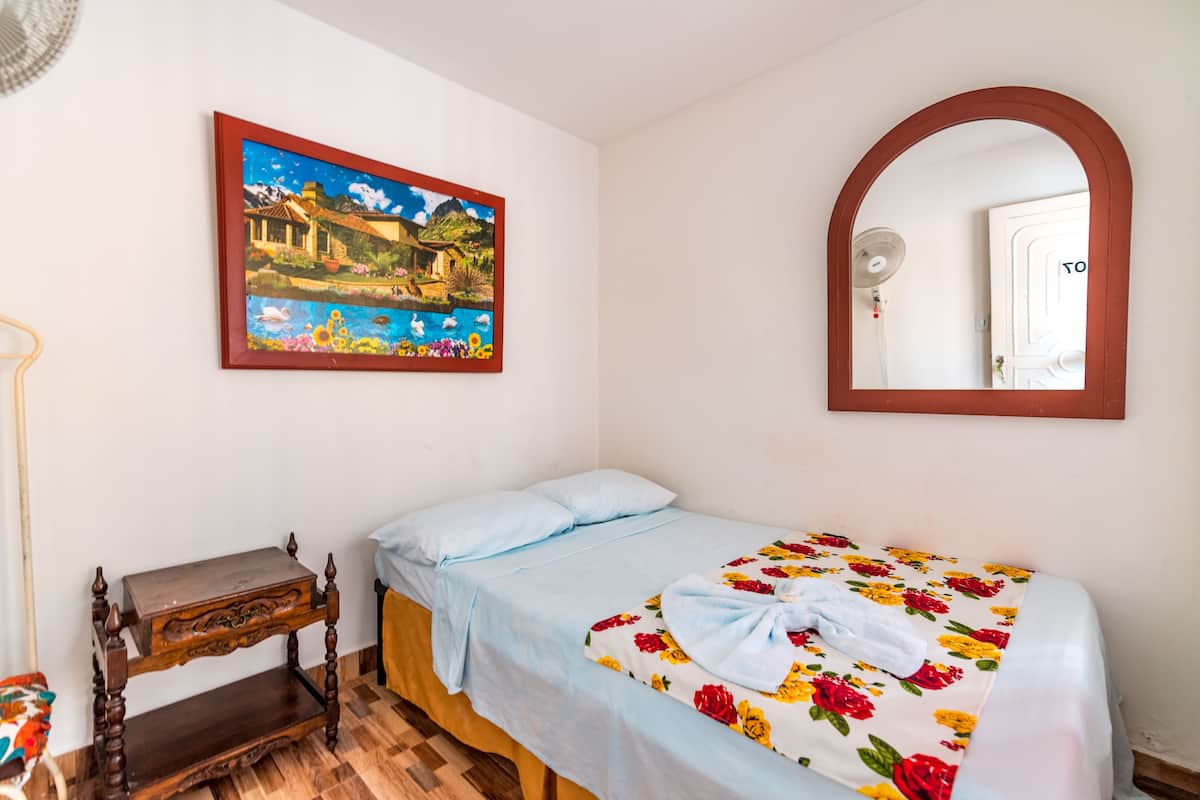 A bedroom with a bed, a wooden nightstand, a painting, and a mirror.