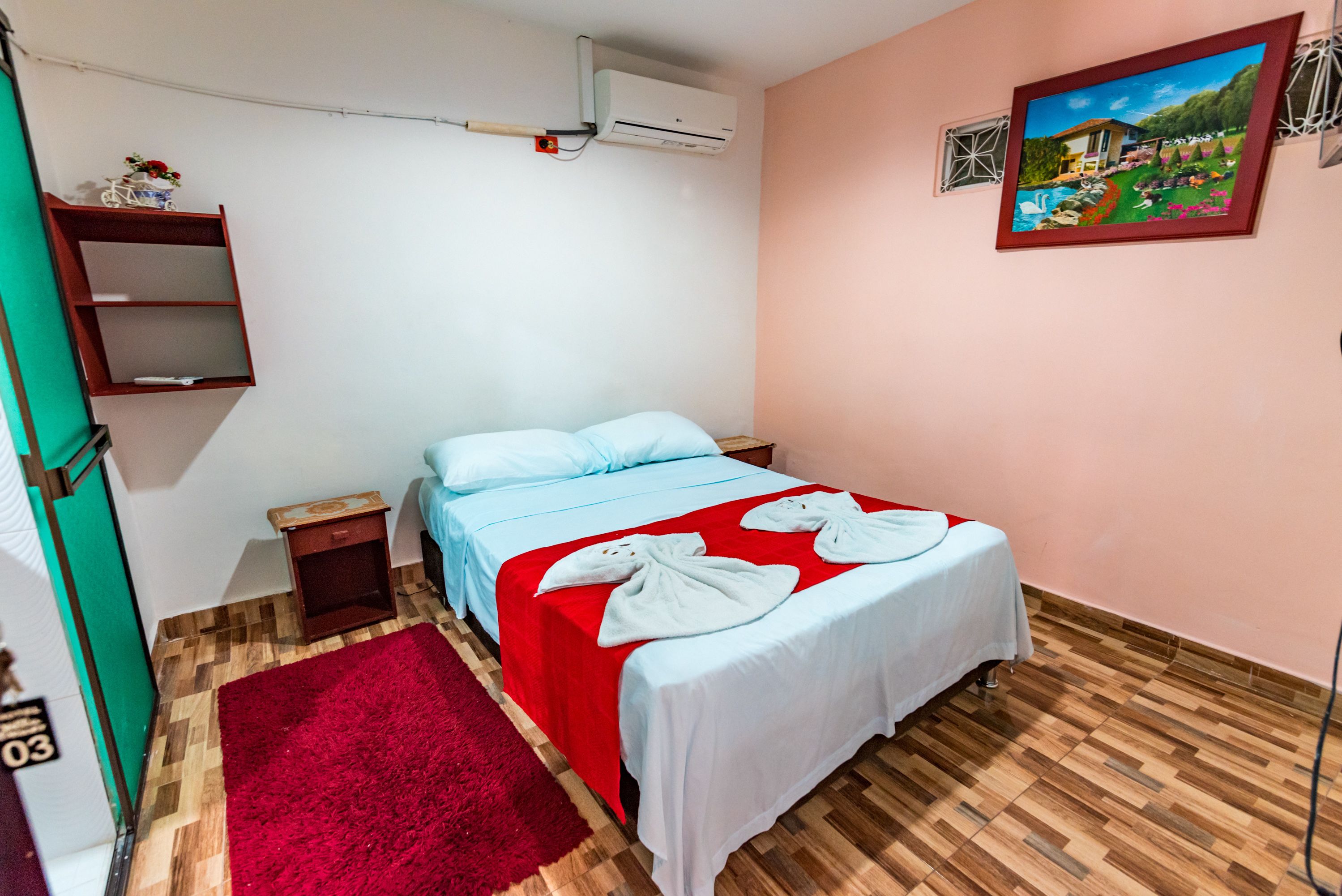 Un dormitorio con una cama, una alfombra roja, una pared blanca y un cuadro.