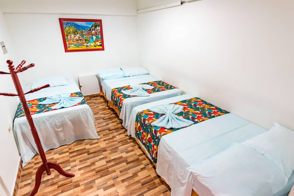 A room with three beds, each with a colorful floral bedspread and white sheets. A wooden chair is positioned in front of the beds.