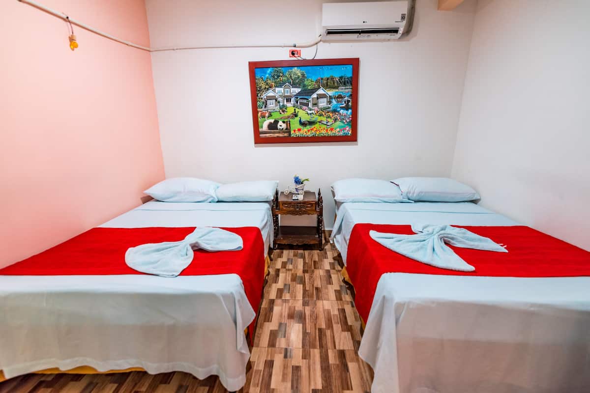 A hotel room with two beds, a wooden floor, a painting on the wall, and an air conditioning unit.