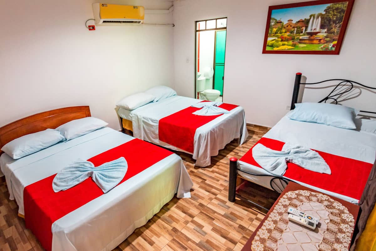 A hotel room with two beds, each with a red bedspread and a white pillow. There is a small table with a remote control on it, and a painting on the wall.