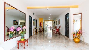 A hotel corridor with a mirrored wall, a reception desk, and a seating area with chairs. - Hotel Villa Deicer (Villavieja)