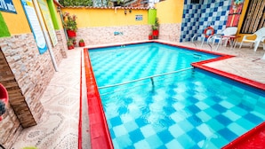 A swimming pool with a red and blue checkered pattern, surrounded by a tiled patio and potted plants. - Hotel Villa Deicer (Villavieja)