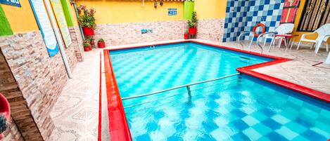 Una piscina con un estampado de cuadros azules y rojos, rodeada por un patio con baldosas y plantas en macetas.