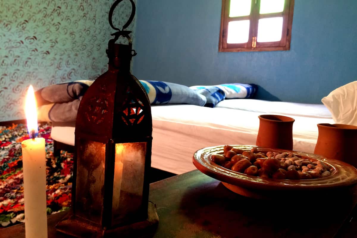 Una habitación con una cama, una vela encendida, un farol y un cuenco de nueces sobre una mesa.