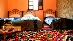 Una habitación con dos camas, una mesita con un farol y una alfombra colorida.