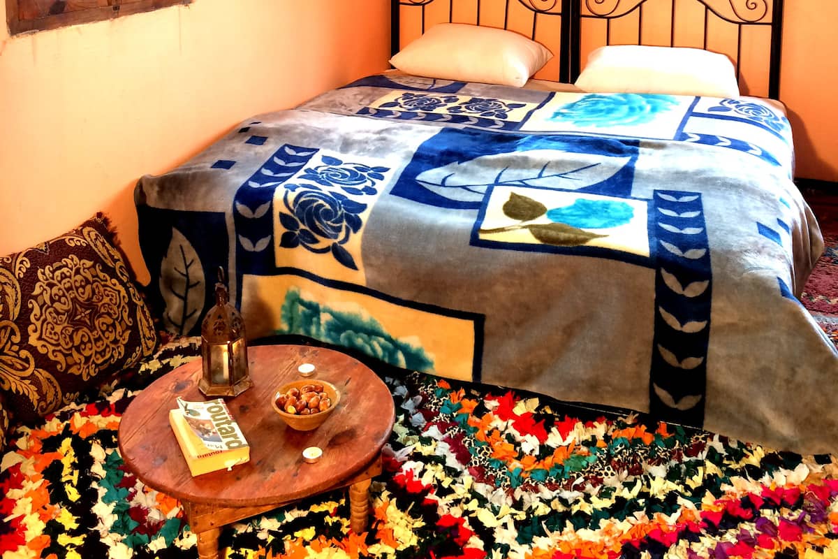 Un dormitorio con cama, mesita de noche, ventana y alfombra estampada.