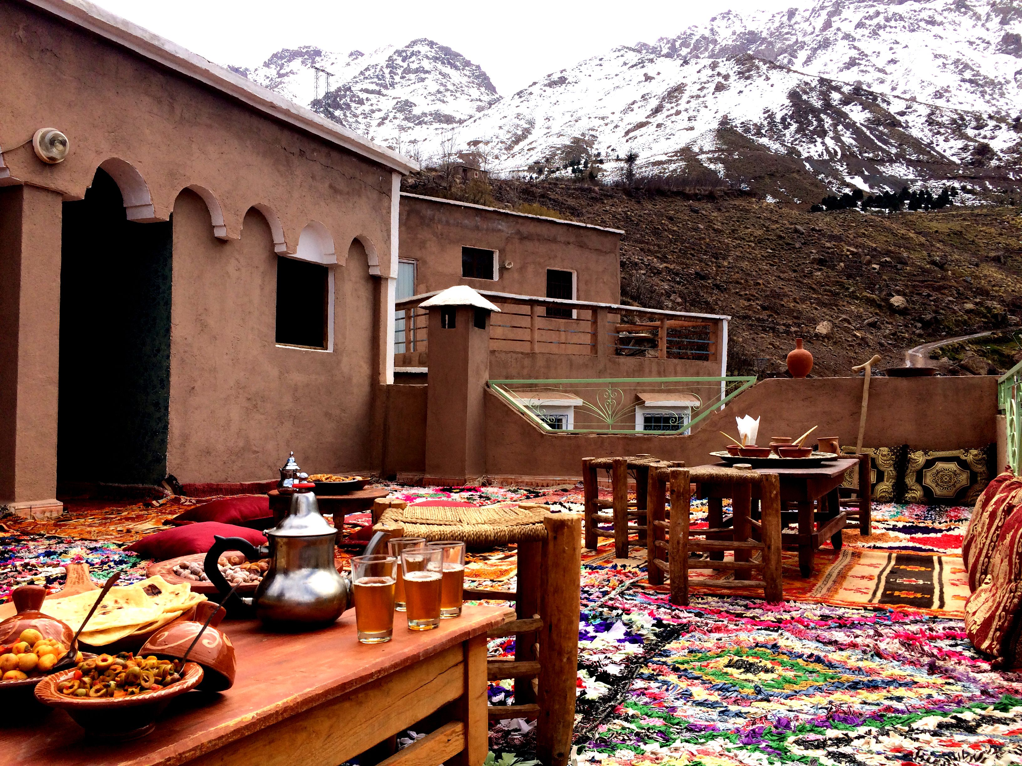 A traditional setting with a table set for dining, a building with arches, and a mountainous backdrop.