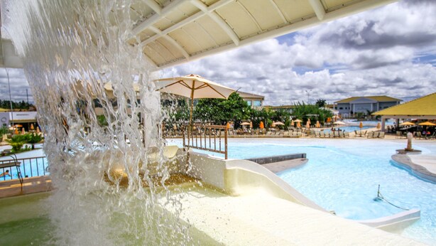Tobogán de agua que desemboca en una piscina con sombrillas y sillas de descanso.