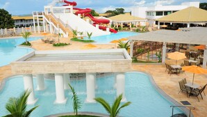 Zona de piscina hotelera con tobogán de agua, asientos exteriores y un área de comedor cubierta.