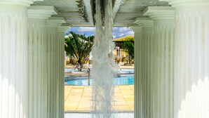 Un área de piscina con fuente de agua, rodeada de columnas y palmeras.