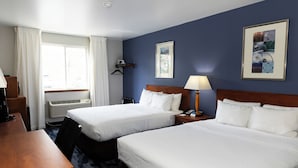 A hotel room with two beds, a desk, a chair, a lamp, and a framed picture on the wall.