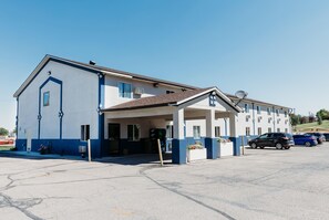 A two-story building with a covered entrance, parking lot, and several parked cars.