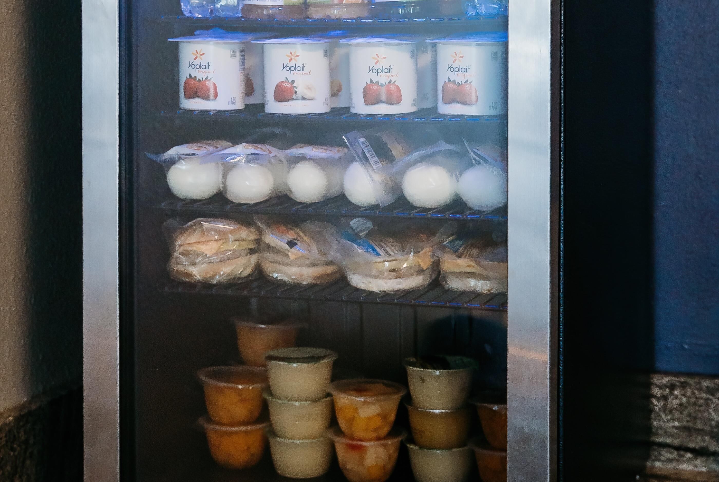 Een koelvitrine met diverse etenswaren, waaronder verpakte yoghurt, brood en drankjes.