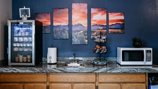 A kitchen with a refrigerator, microwave, sink, and a wall with four sunset paintings.