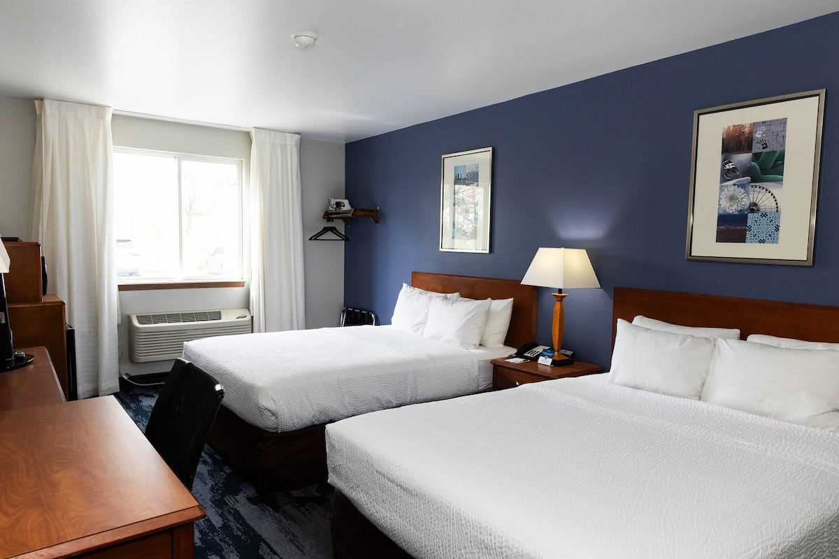 A hotel room with two beds, a desk, a chair, a lamp, and a window with curtains.