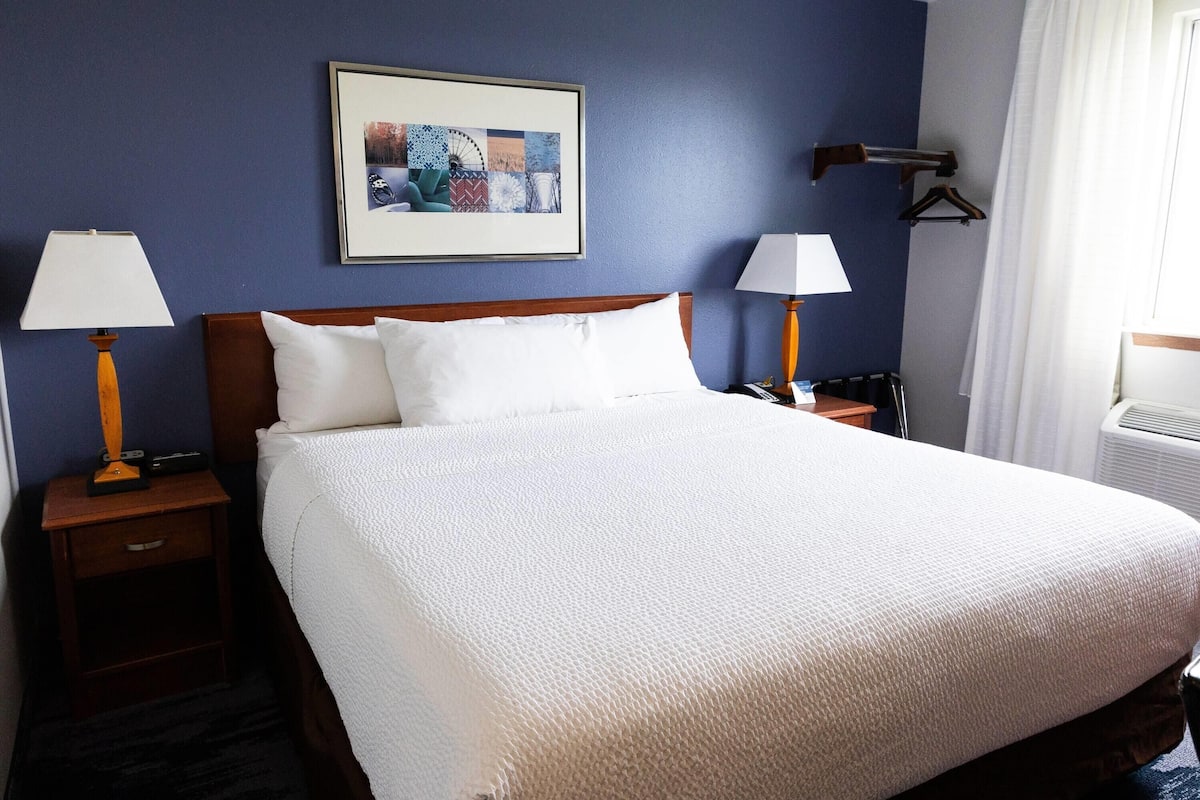 A hotel room with a large bed, two bedside tables with lamps, a framed picture on the wall, and a window with curtains.