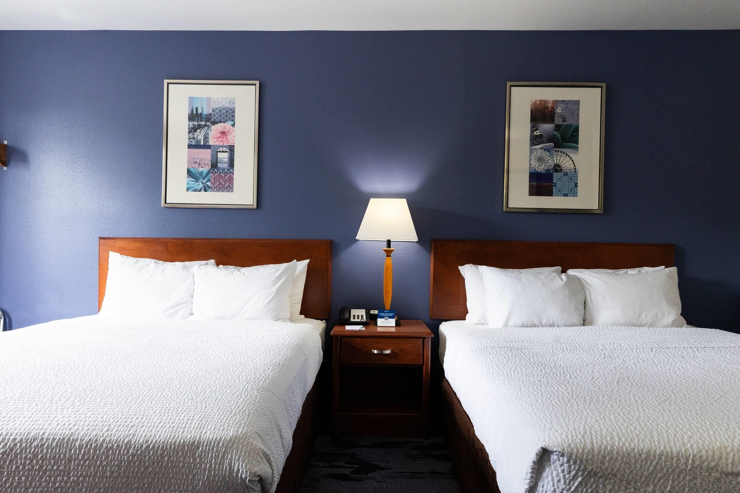 Ein Hotelzimmer mit zwei Betten, einem Nachttisch mit Lampe und zwei gerahmten Bildern an der Wand.