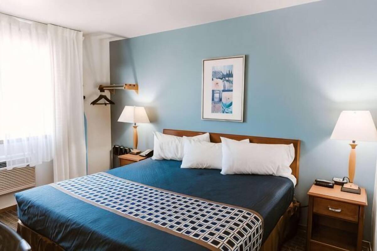 A hotel room with a bed, two bedside tables, a nightstand, a window with curtains, and a wall-mounted picture.
