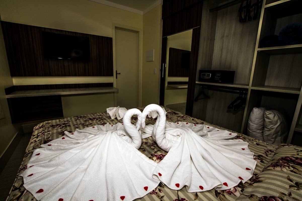 A hotel room with a bed, a TV mounted on the wall, a wardrobe, and a mirror.