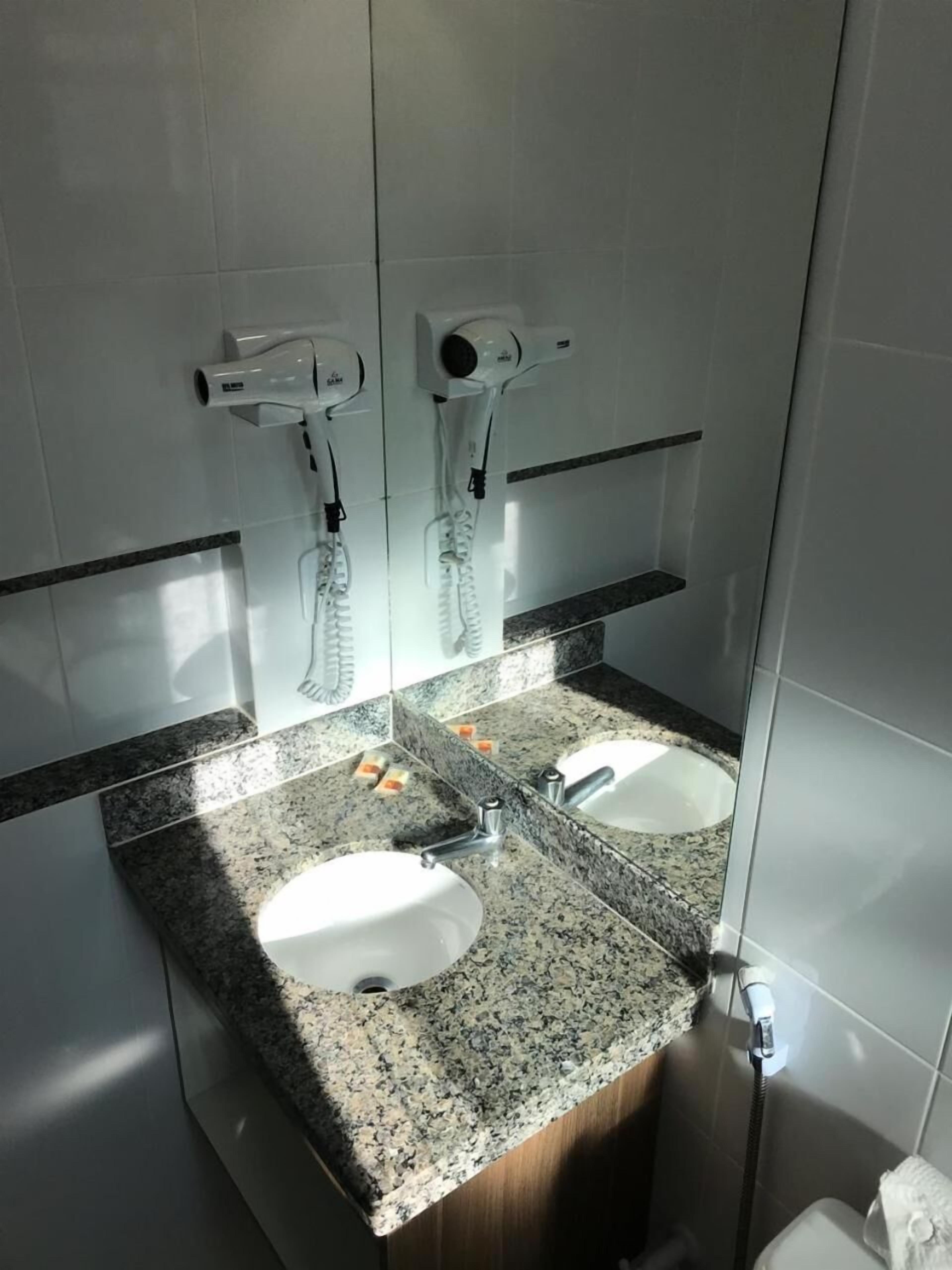 A bathroom with two sinks, a mirror, and a hairdryer mounted on the wall.