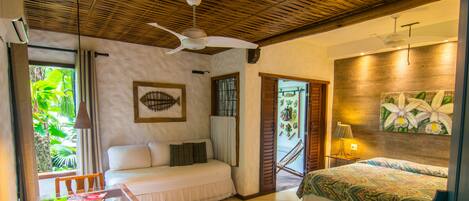 A room with a bed, a sofa, a dining table, and a ceiling fan.
