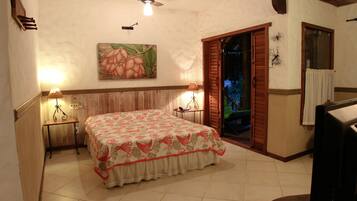 A bedroom with a bed, two bedside lamps, a ceiling fan, a painting on the wall, and a window with shutters.